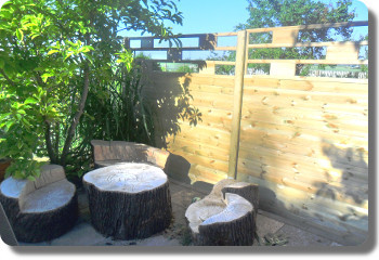 Sichtschutzzaun mit Zierelement im Garten hinter einer Sitzgruppe mit Baum